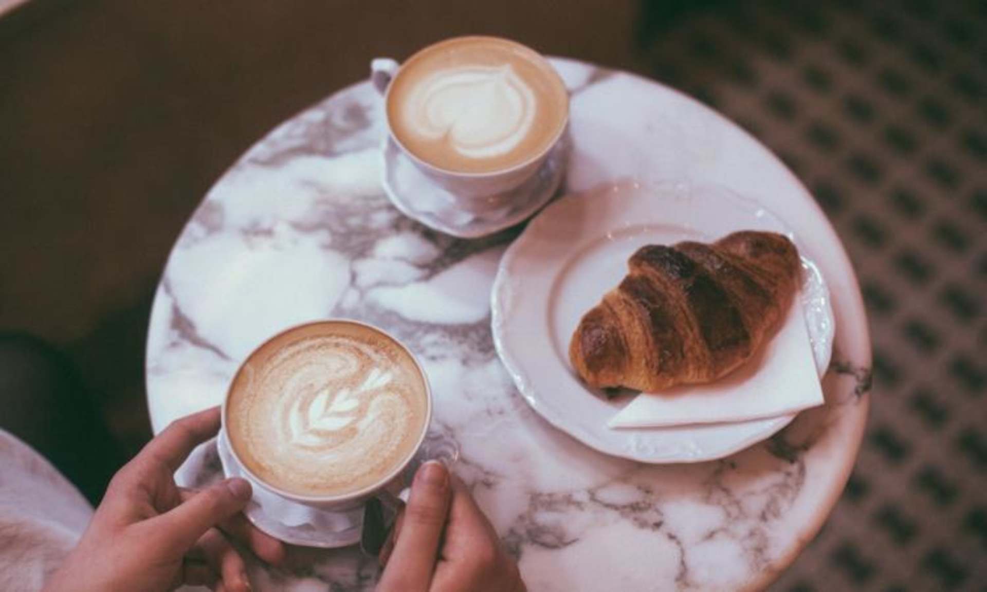 A marble-patterned plate holds two steaming cups of coffee and a freshly baked croissant, creating a cozy and inviting scene.
