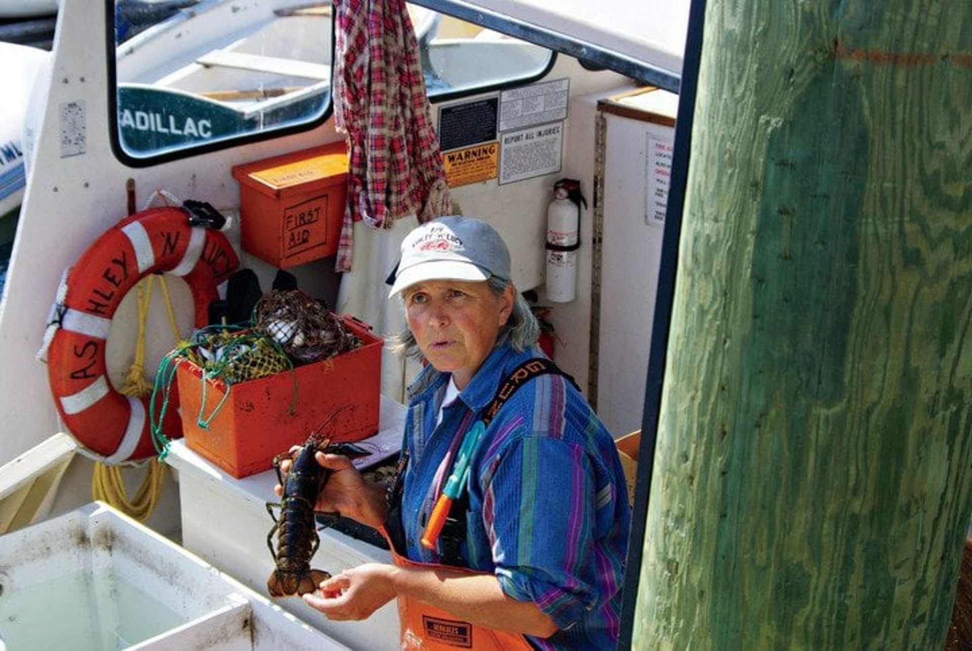 An elderly person wearing a colorful jacket and hat is standing in the interior of what appears to be a small boat or vessel, surrounded by various nautical equipment and supplies.