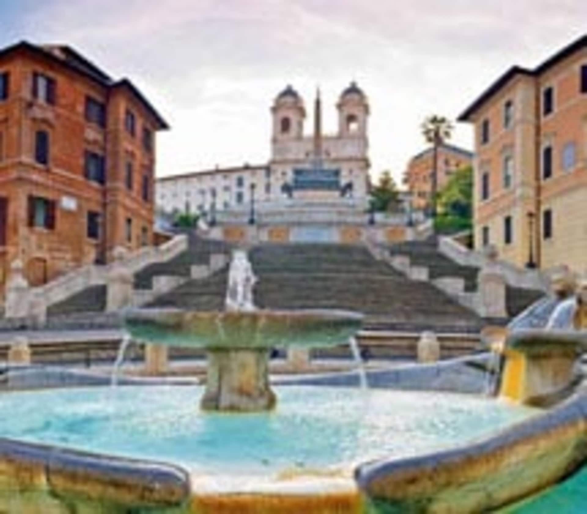 A grand staircase leads up to a historic church, with a fountain in the foreground and colorful buildings surrounding the scene.