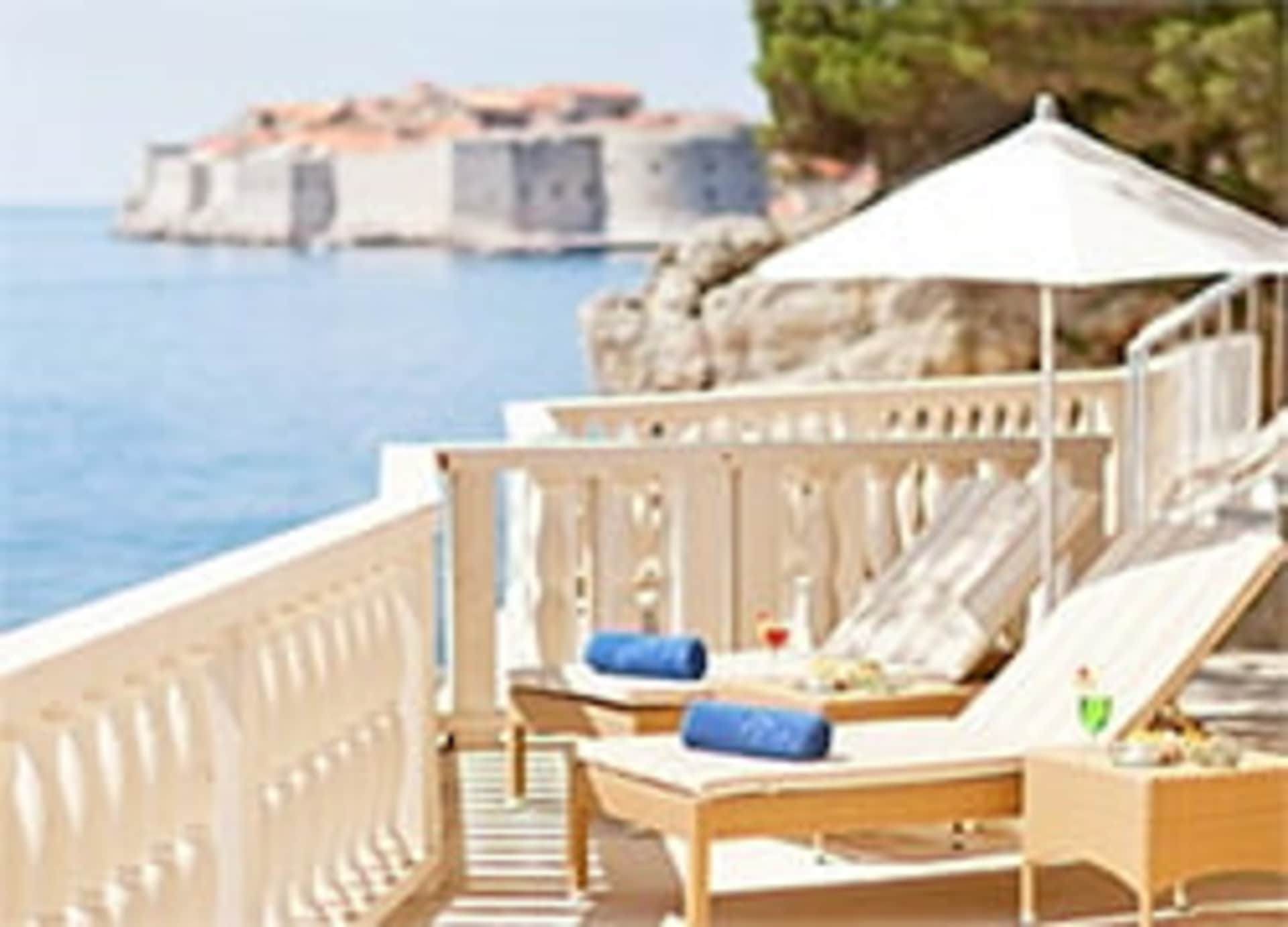 A wooden deck with lounge chairs overlooking a scenic coastal town with buildings and the sea in the background.
