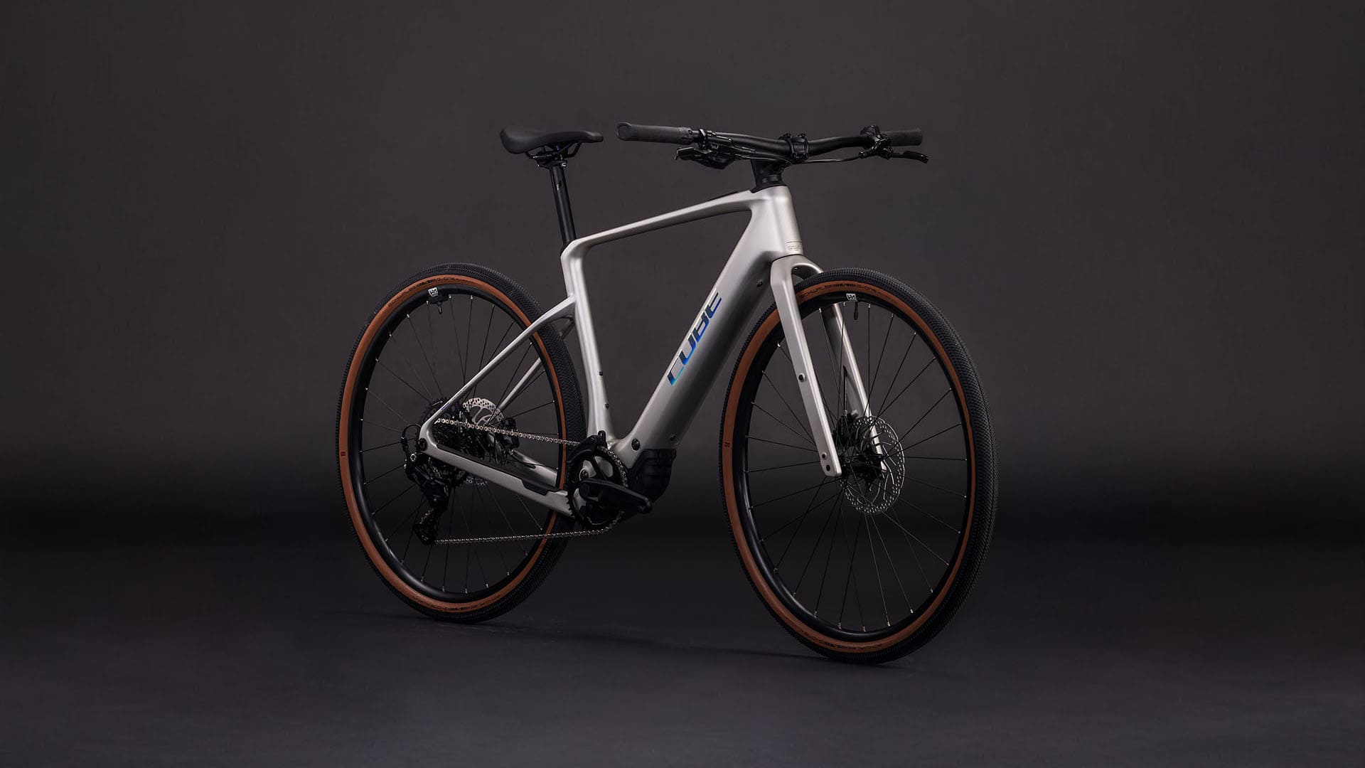 A sleek, modern bicycle with a silver frame and black components stands against a dark background, its minimalist design and high-quality components suggesting a premium, performance-oriented model.