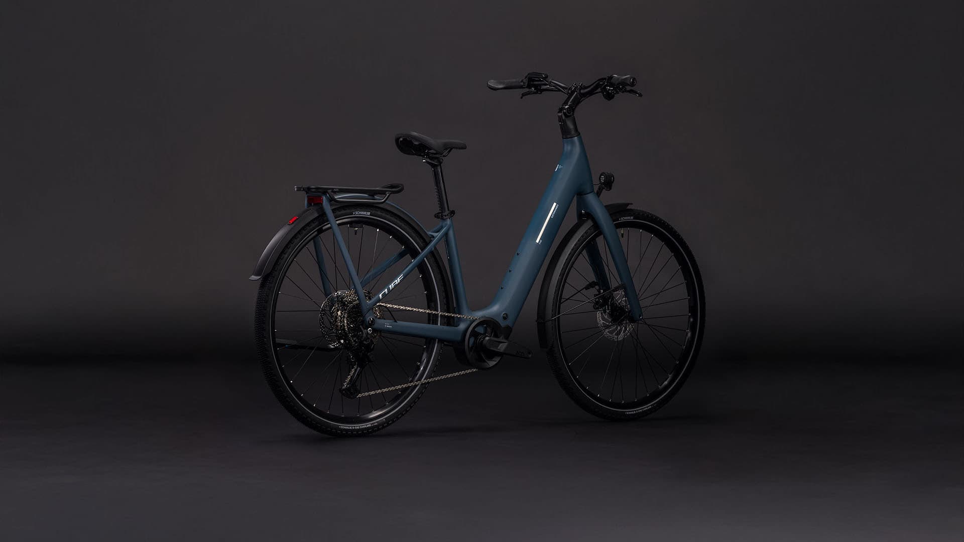 A sleek, modern electric bicycle stands alone in a dark, minimalist setting, its blue frame and black components creating a striking visual contrast.