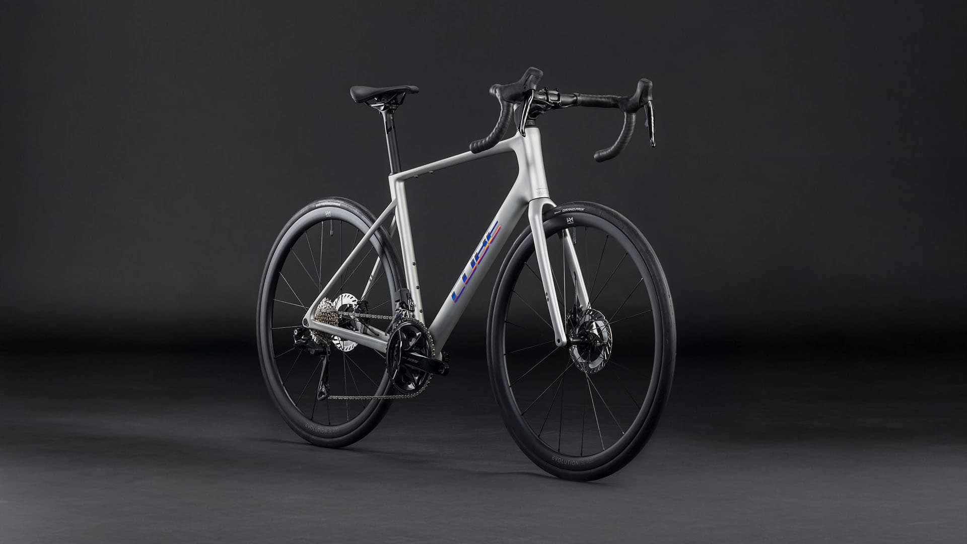 A sleek, modern road bicycle with a white frame and black components stands against a dark background, its clean lines and minimalist design creating a striking visual impression.