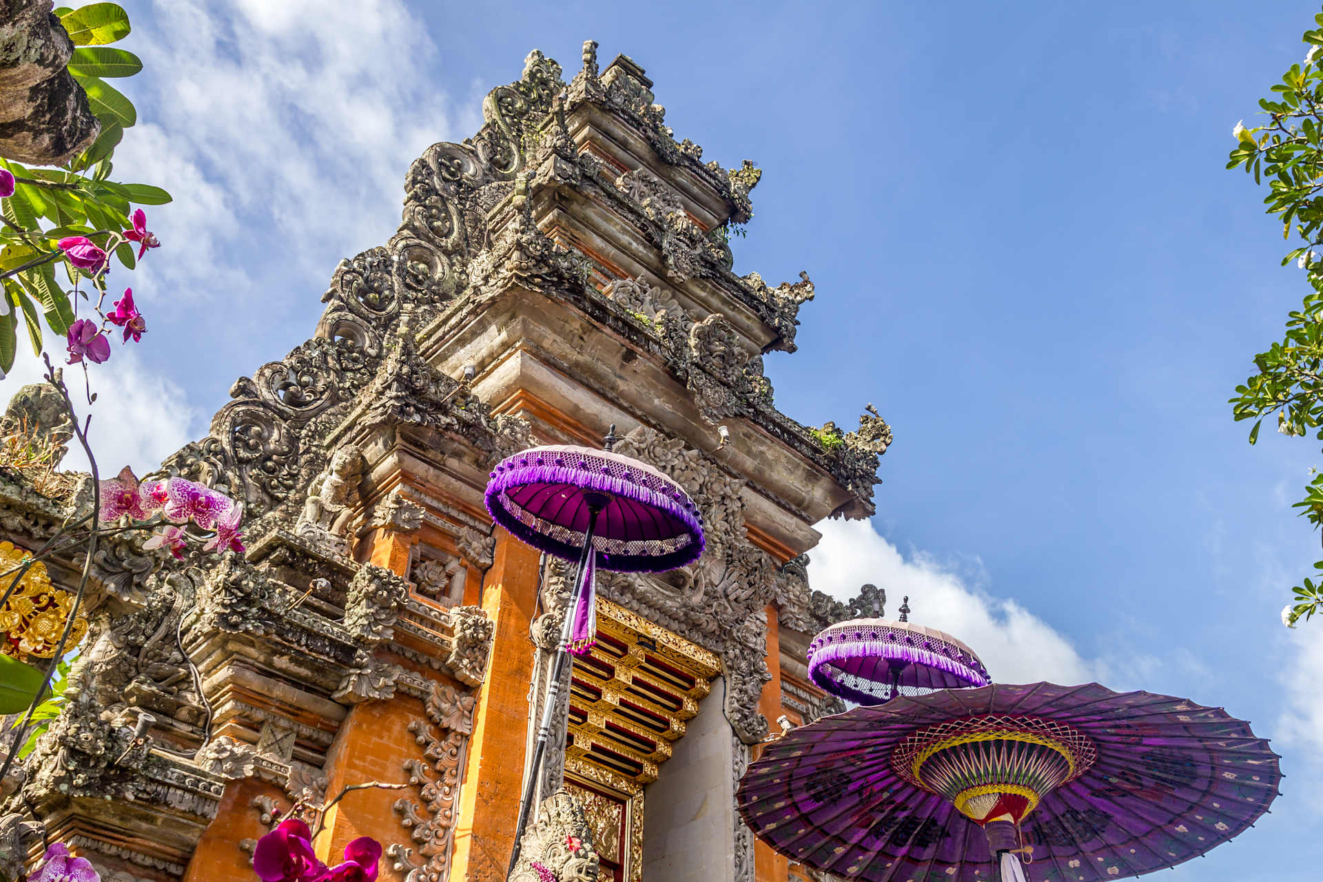 A colorful and ornate temple structure with intricate carvings and decorations, surrounded by lush greenery and vibrant flowers in the foreground.