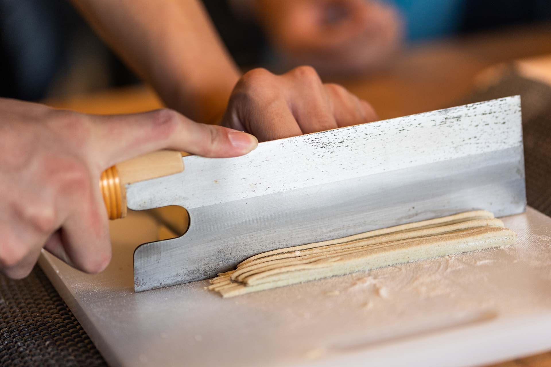 Hands are using a wooden rolling pin to roll out dough on a floured surface.