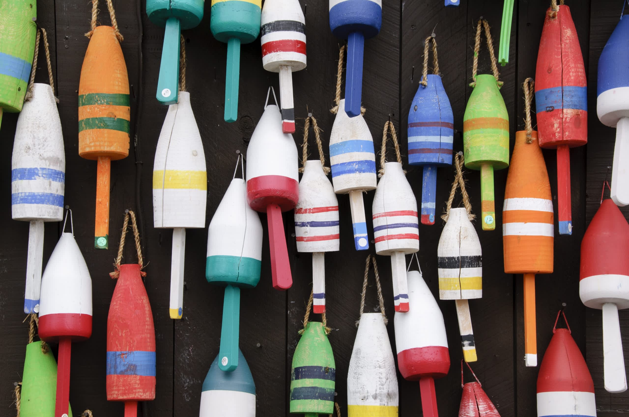 A collection of colorful, weathered fishing buoys or floats, arranged in a dense, overlapping pattern against a dark background.