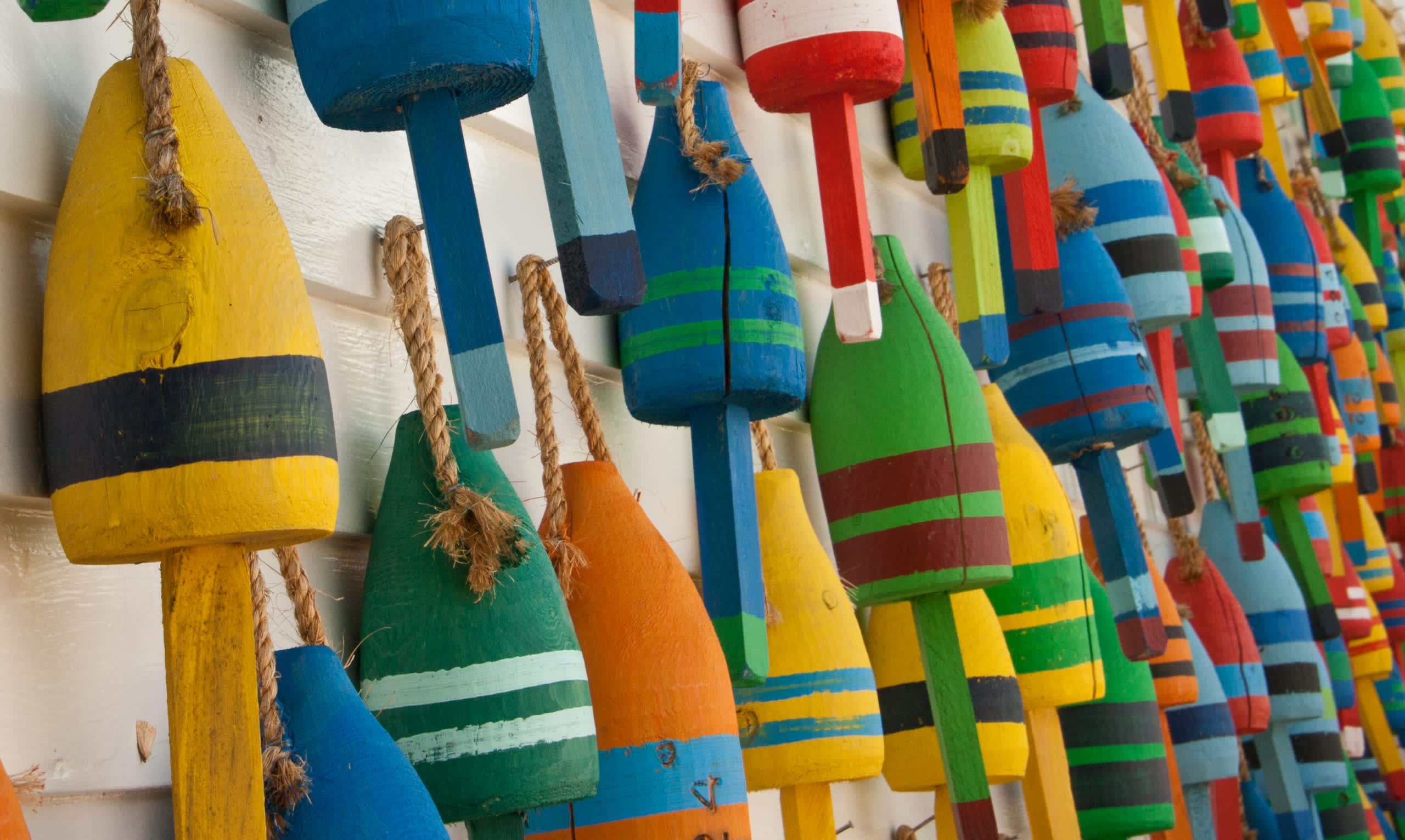 Colorful, wooden buoys or floats hang in a row, creating a vibrant and playful display against a plain white background.