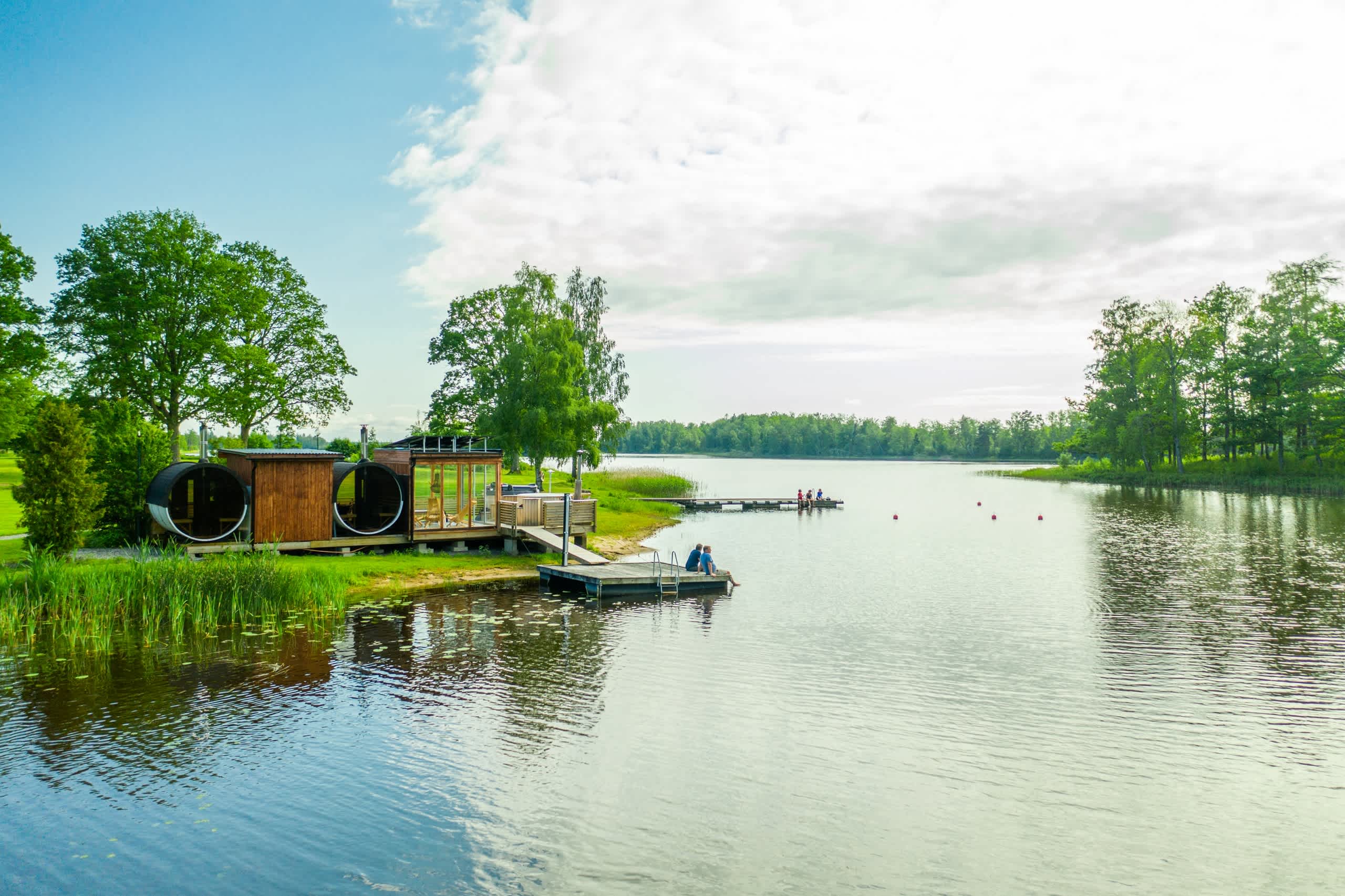 A serene lake surrounded by lush greenery, with a wooden dock and small structures in the foreground, creating a peaceful and tranquil scene.