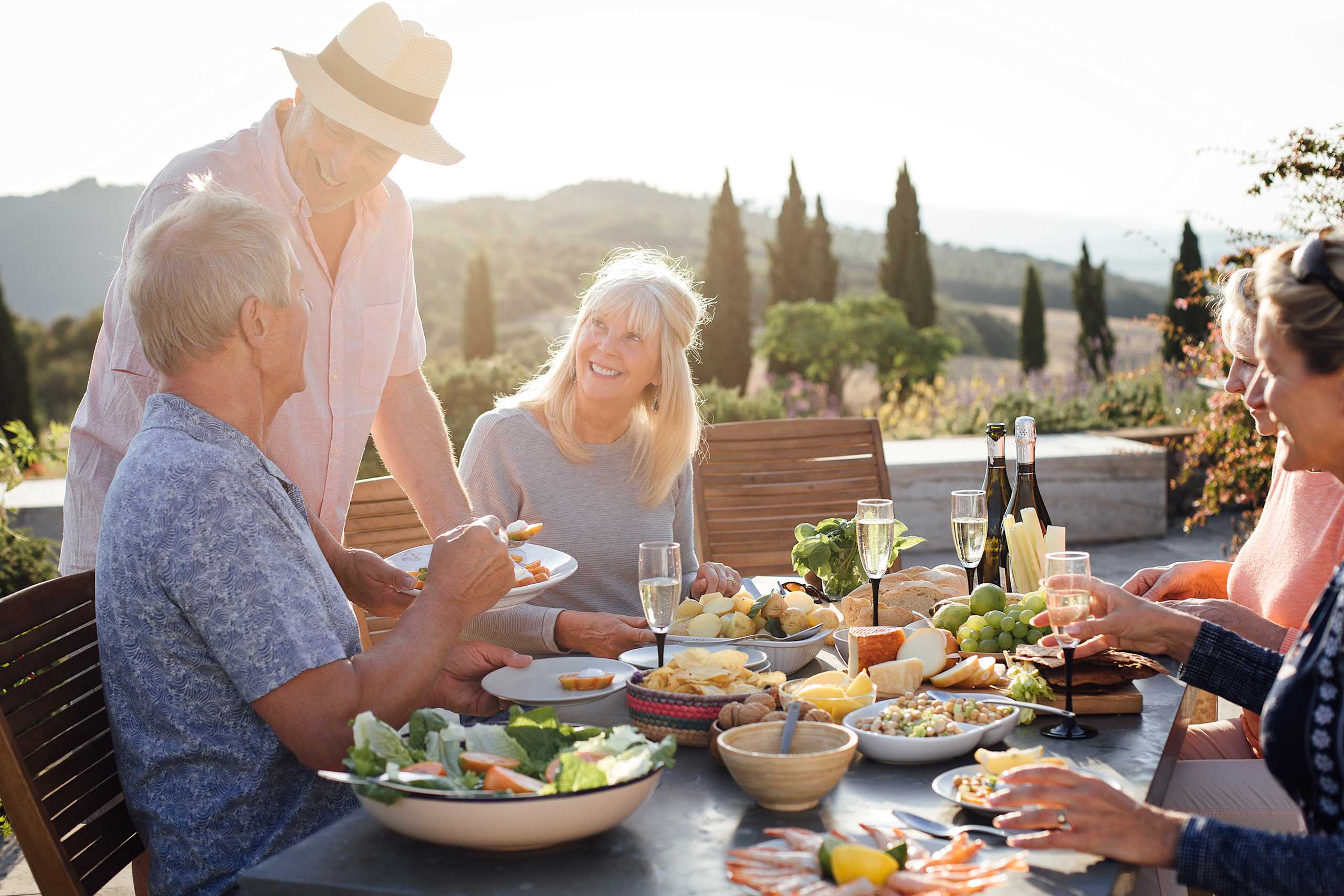 A group of people enjoying an outdoor meal together on a sunny day, surrounded by a lush, scenic landscape.