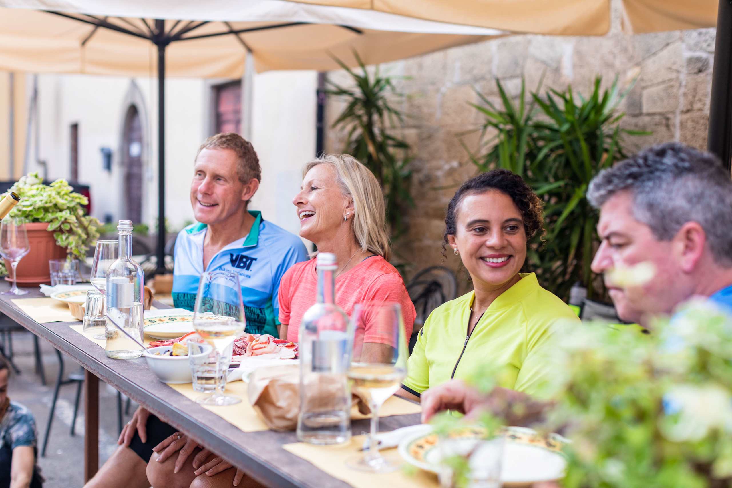 A group of people enjoying a meal together outdoors, surrounded by lush greenery and a cozy patio setting.