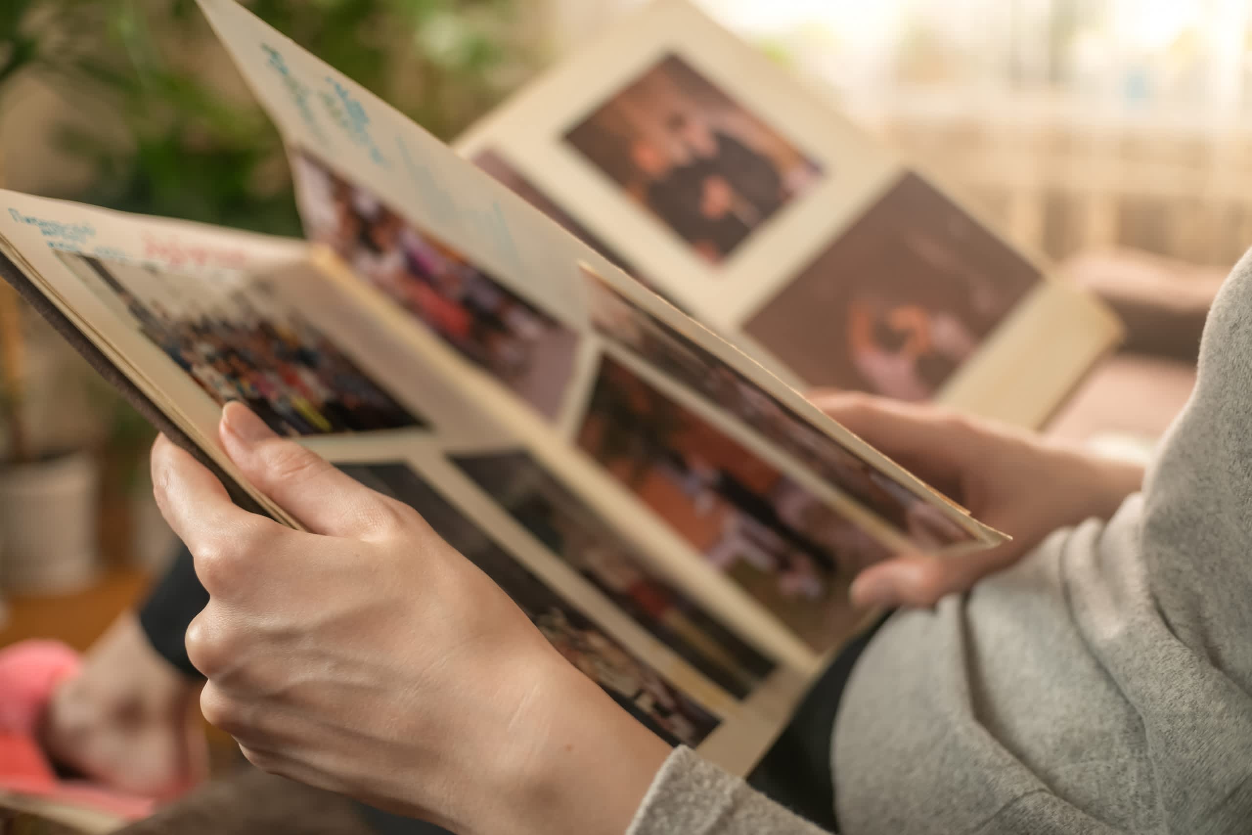 The image shows a person's hands holding a collection of old photographs, with a blurred background suggesting a cozy, domestic setting.