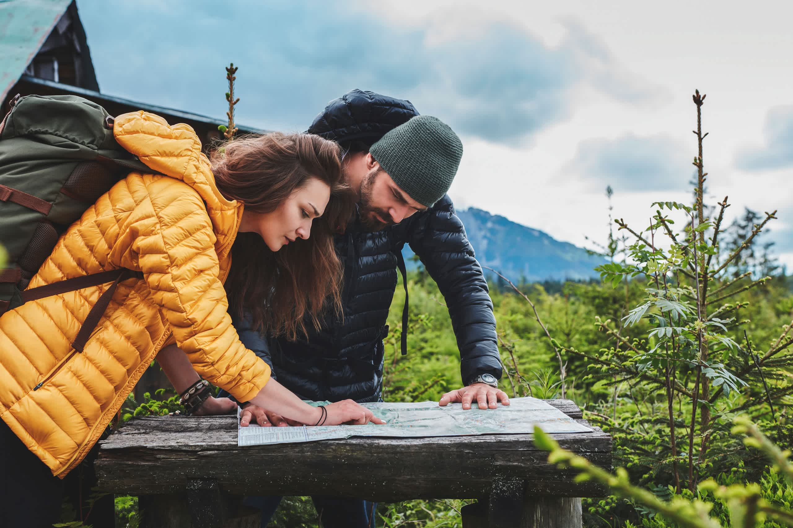 Two people, a man and a woman, are embracing on a wooden platform in a scenic outdoor setting with mountains and greenery in the background.
