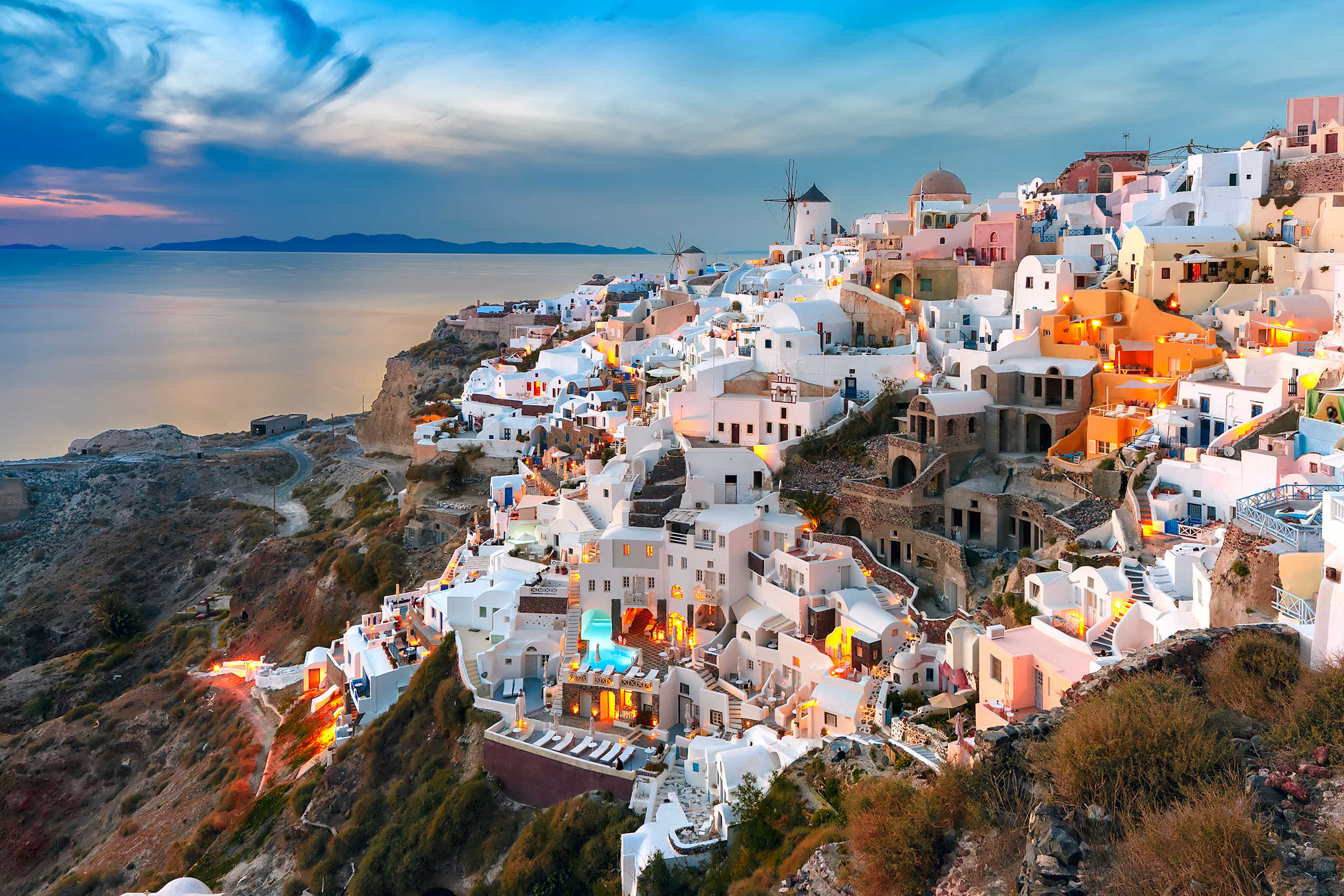 A picturesque coastal town with whitewashed buildings cascading down a hillside, set against a vibrant blue sky and serene waters in the background.