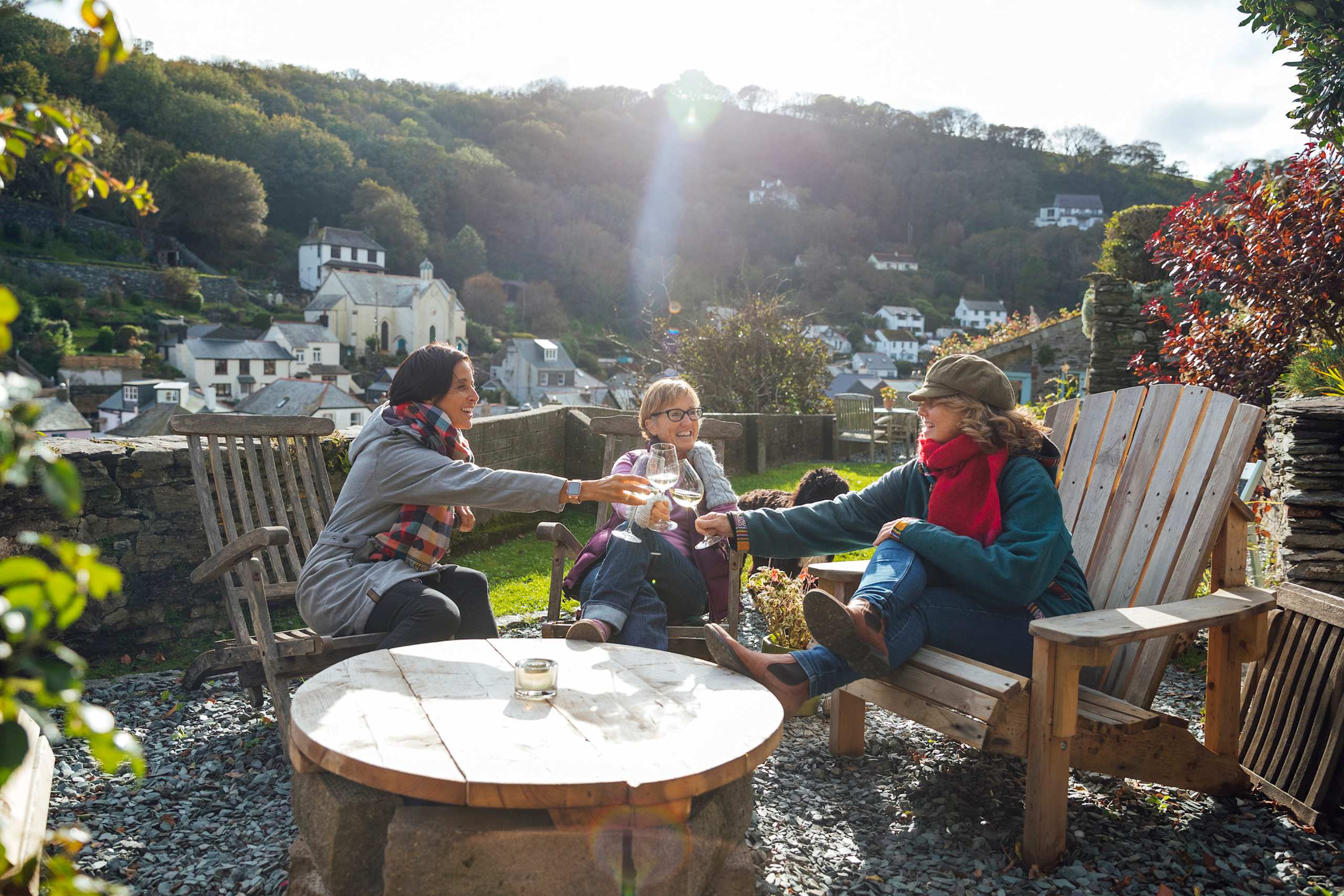 A group of people enjoying a cozy outdoor gathering in a scenic village setting, surrounded by lush greenery and picturesque buildings in the background.