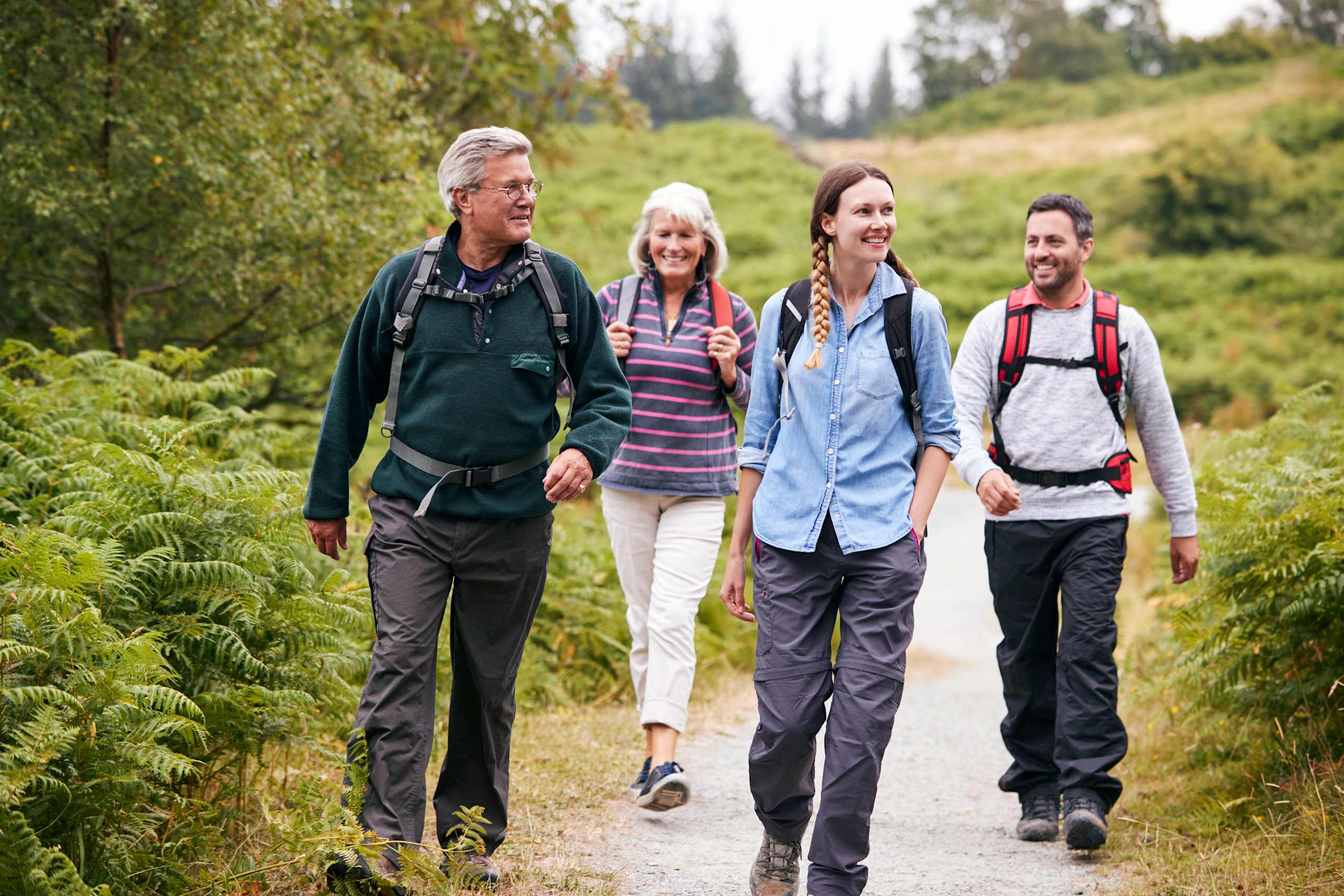 A group of four people, two men and two women, are walking together on a path surrounded by lush, green vegetation in a forest setting.