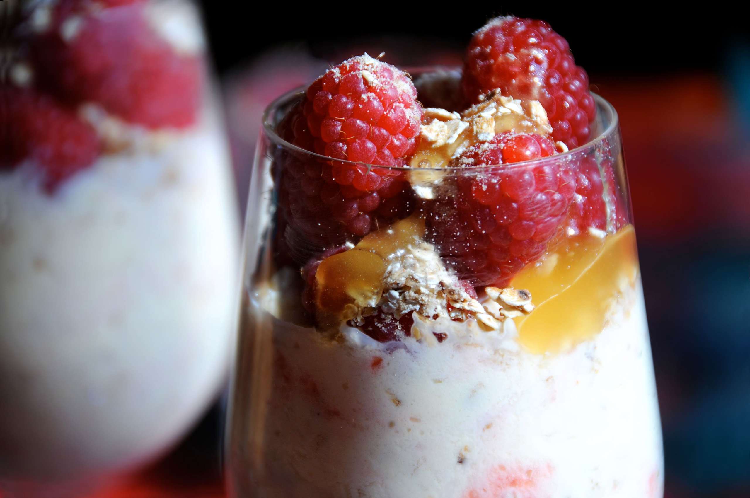 A glass filled with layers of creamy white yogurt, fresh red strawberries, and crunchy granola, set against a blurred background.