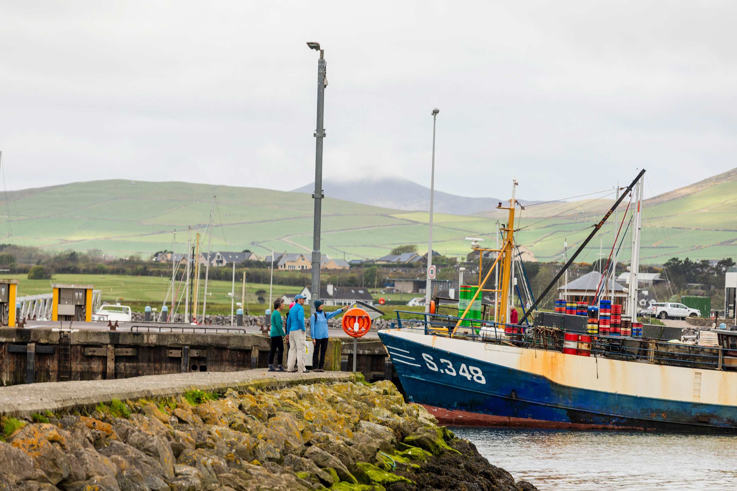 A fishing boat docked in a harbor, with mountains and hills visible in the background.