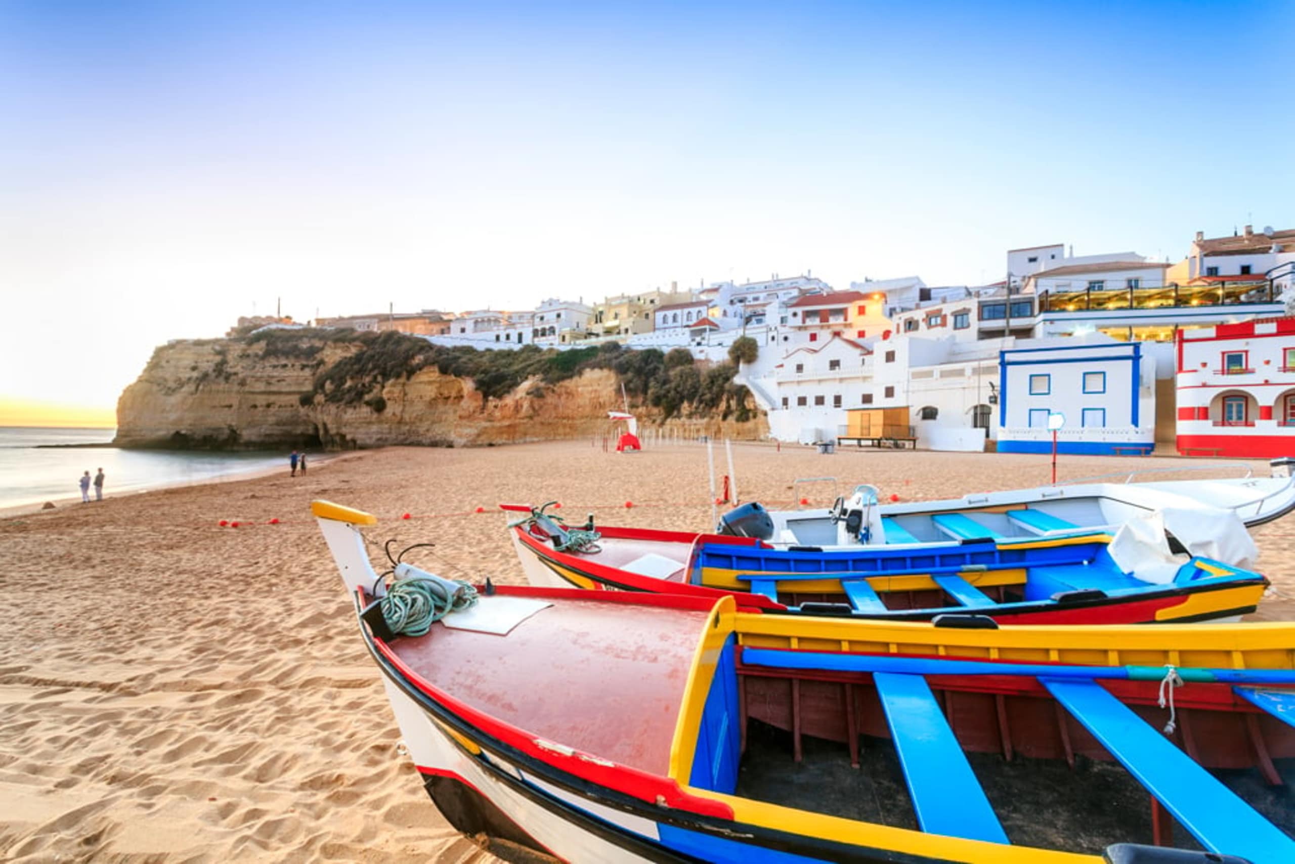 A colorful fishing boats on a sandy beach, with a picturesque coastal town nestled on the cliffs in the background.