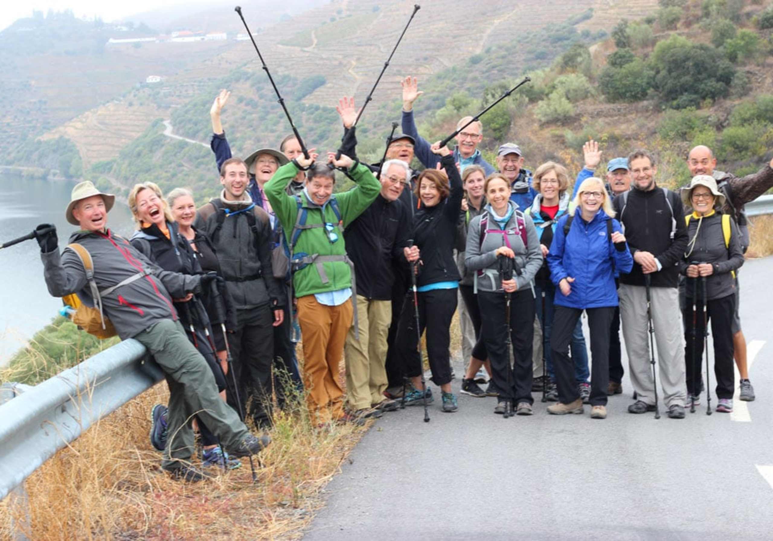 A group of people, dressed in outdoor gear, standing together on a path overlooking a scenic mountainous landscape.