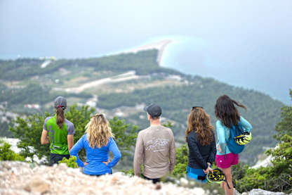 Group of cyclists standing on a high viewpoint in Croatia, looking out over a forested peninsula and the turquoise coastline below.