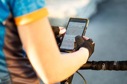 Cyclist checks the voice navigation app on their phone, reviewing route details and voice-navigation cues while stopped on the bike.