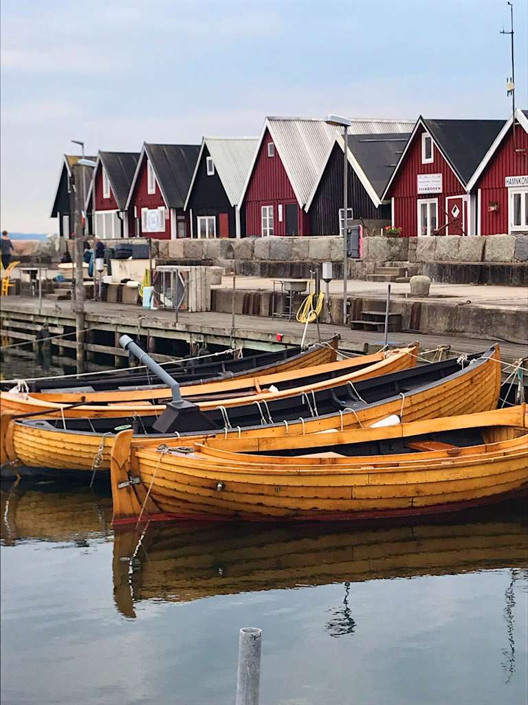 Colorful wooden houses line the shore, with several traditional wooden boats moored in the calm waters in the foreground.