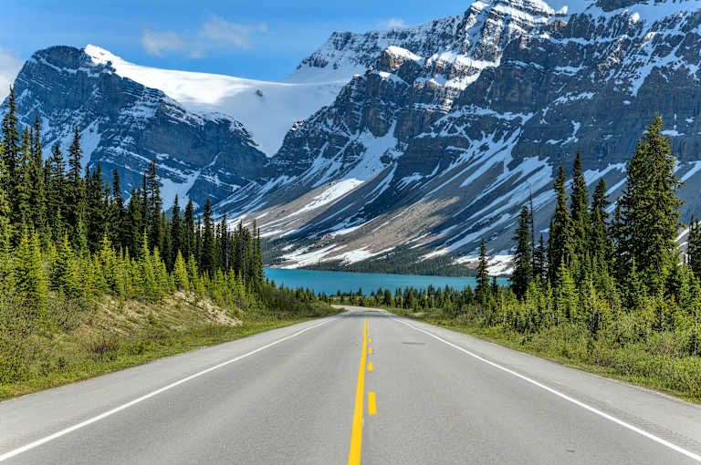 A Spring evening view of Icefields Parkway extending towards Bow Lake, with BowCrow Peak, Crowfoot Glacier and Crowfoot Mountain rising high behind, Banff National Park, AB, Canada.