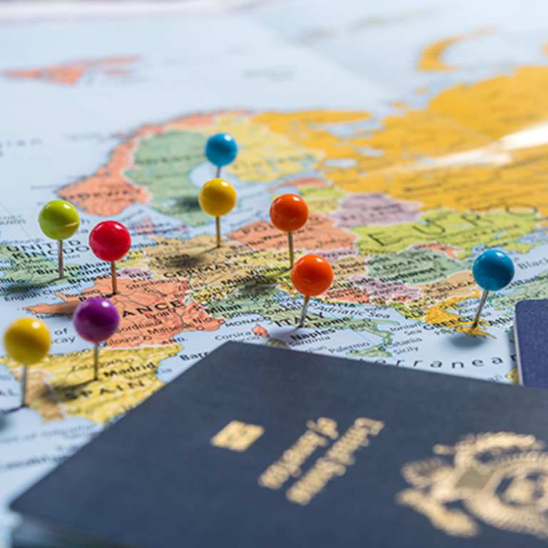 Colorful pushpins are placed on a map, with a passport visible in the foreground, suggesting travel and exploration.