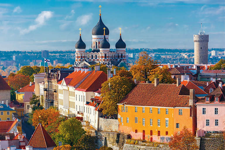 A vibrant cityscape with colorful buildings, a grand cathedral with onion-shaped domes, and a tower in the background, all set against a clear blue sky with fluffy clouds.