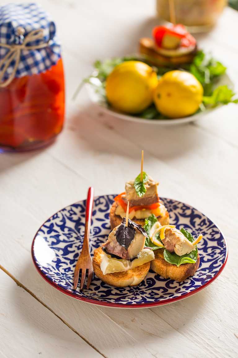 A delicious-looking burger with various toppings sits on a patterned plate, accompanied by a salad and a jar of what appears to be pickled vegetables in the background.