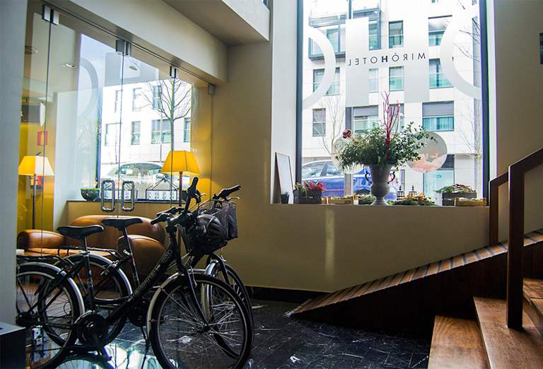 A cozy interior space with a window overlooking a city street, featuring a collection of bicycles, lamps, and other decor elements.