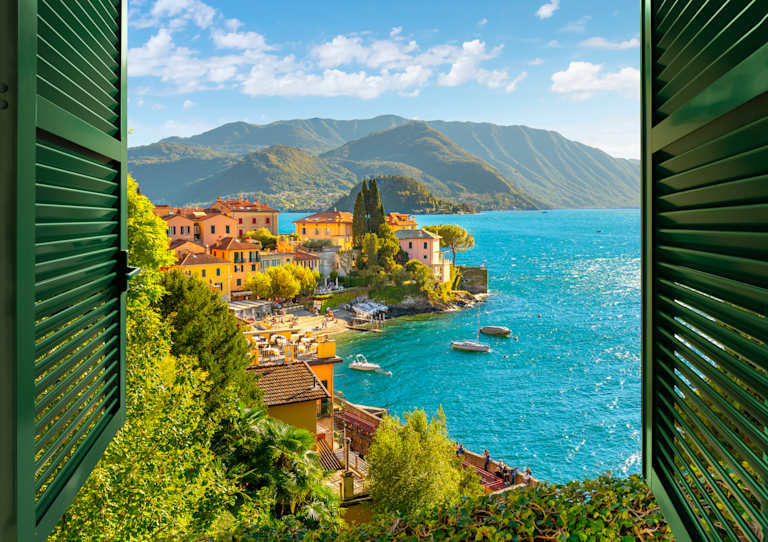 A picturesque coastal town nestled between lush greenery and towering mountains, with vibrant buildings and a serene azure sea in the background.