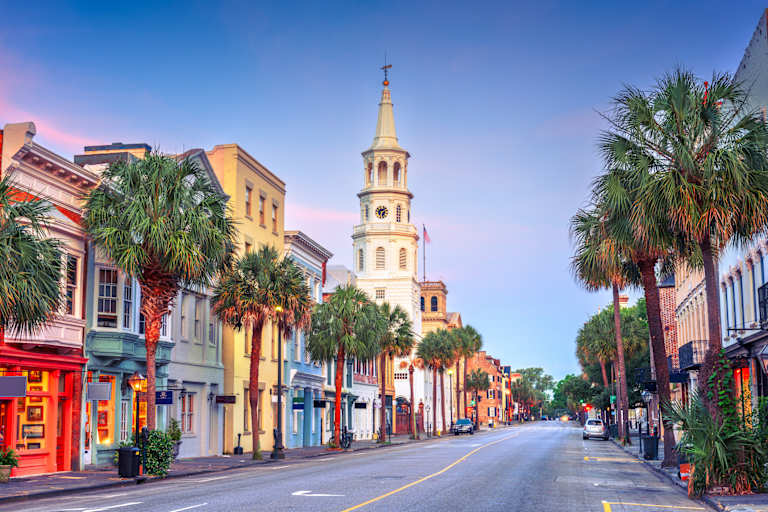 A vibrant street scene with colorful buildings, palm trees, and a tall church steeple in the background, creating a picturesque and lively atmosphere.