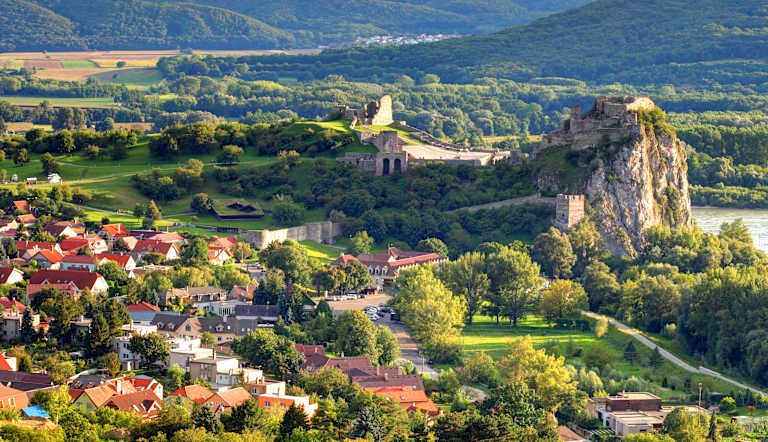 A picturesque village nestled in a lush, mountainous landscape, with a medieval castle perched atop a towering cliff overlooking the scene.