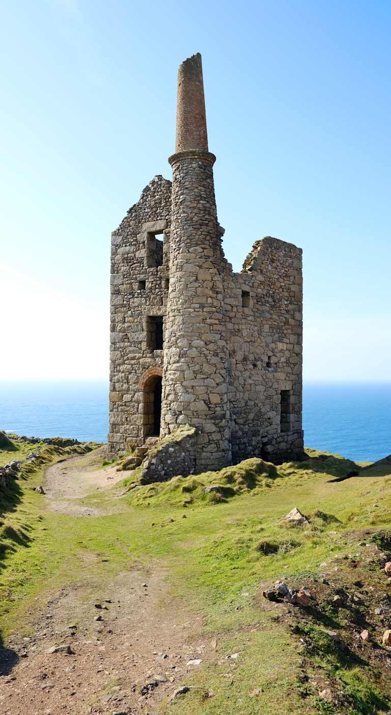 A ruined stone tower stands atop a grassy hill, overlooking the vast expanse of the ocean in the background.