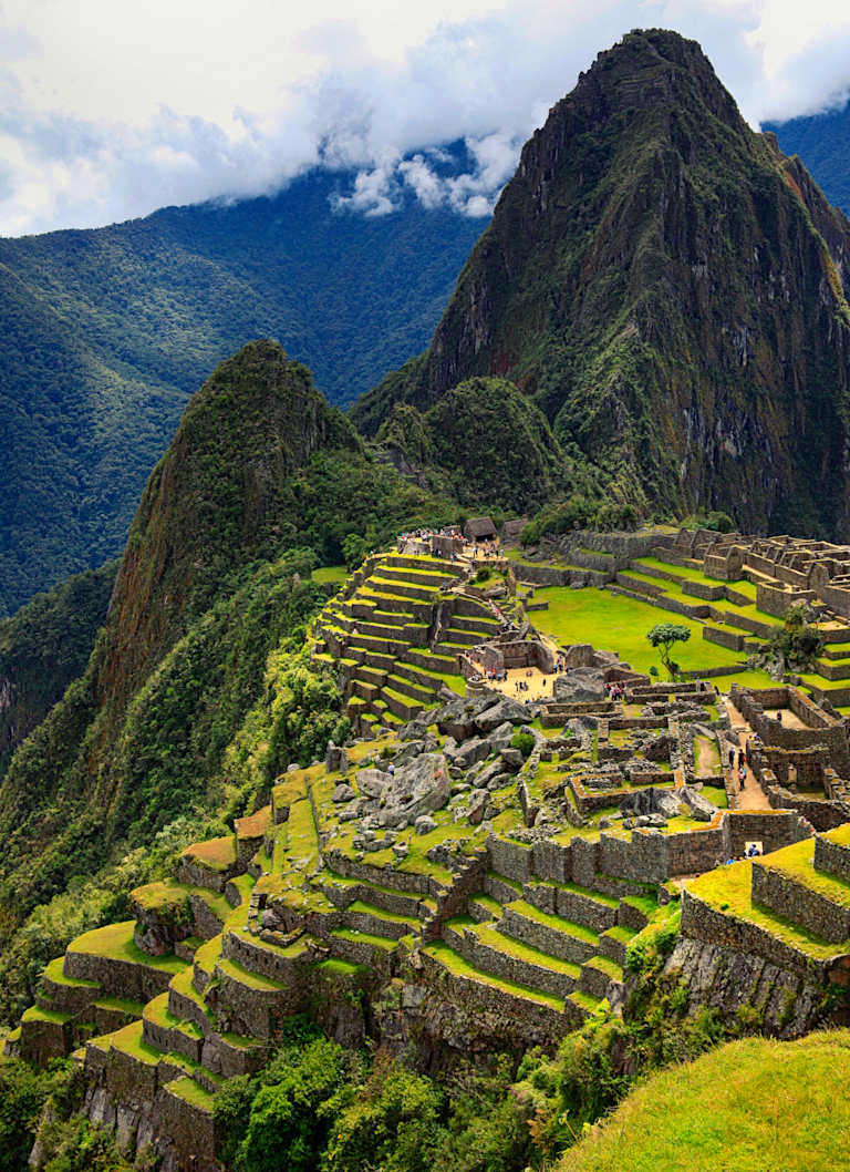 A lush, terraced landscape nestled between towering mountains, with ancient ruins and structures scattered throughout the verdant terrain.