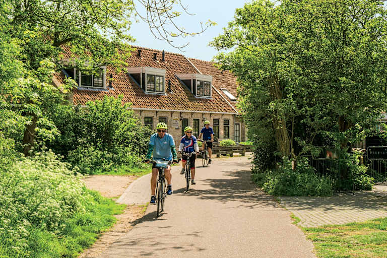 A scenic path winds through a lush, green landscape, with a charming building and cyclists enjoying the outdoors in the background.