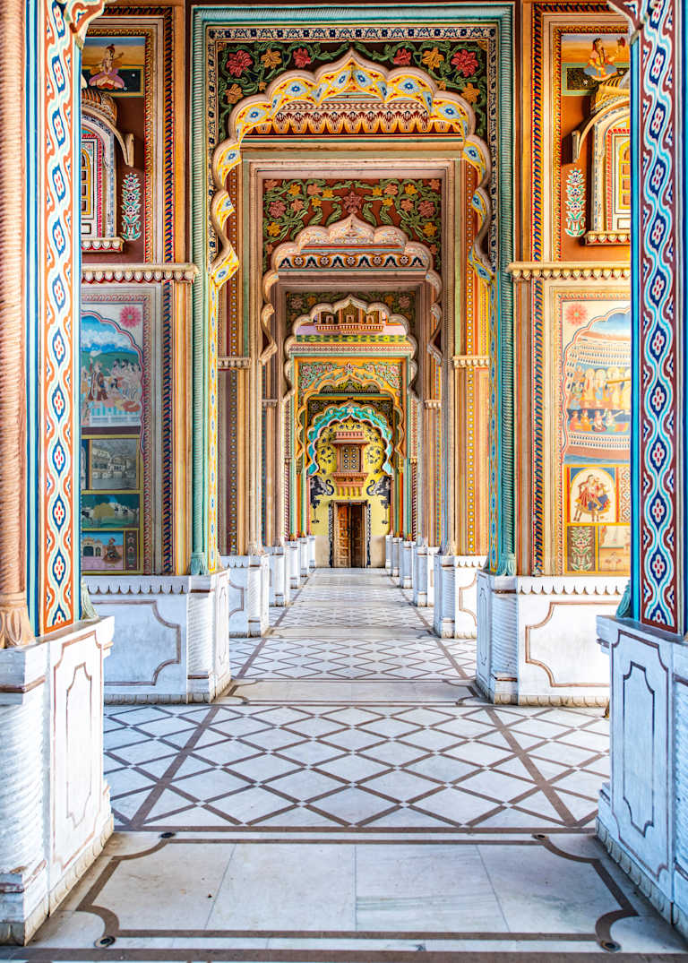 A grand, ornately decorated archway leads into a spacious, tiled corridor with intricate patterns and vibrant colors adorning the walls and ceilings.