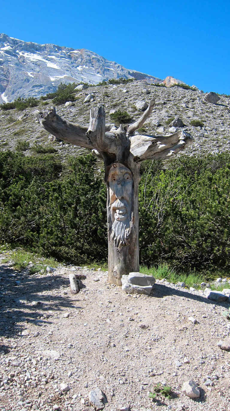 A large wooden sculpture of a deer or stag stands in the foreground, surrounded by a rocky, mountainous landscape in the background.