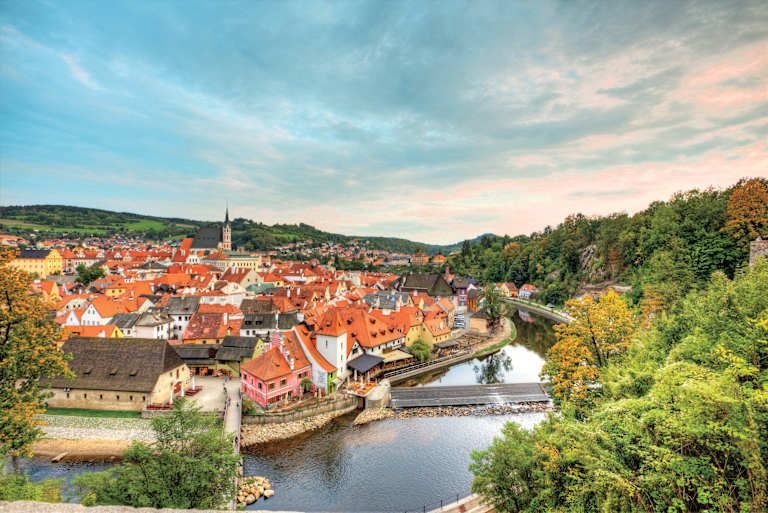 A picturesque town nestled in a valley, with colorful rooftops, a winding river, and lush forests surrounding it, creating a serene and charming landscape.