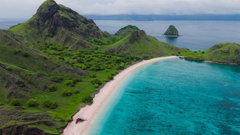 A stunning tropical landscape with lush green mountains, a pristine white sand beach, and crystal clear turquoise waters in the foreground, set against a backdrop of dramatic rocky peaks.