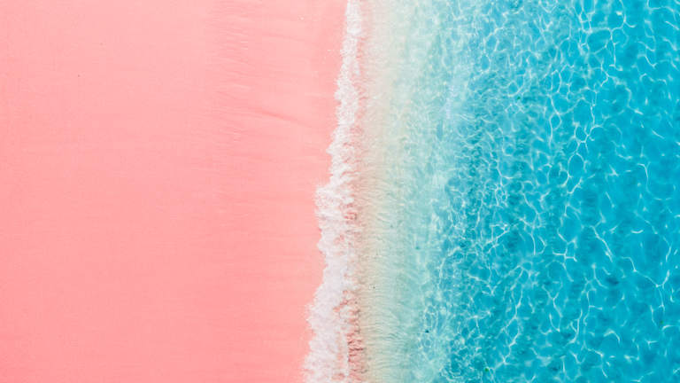 A vibrant pink beach meets the crystal-clear turquoise waters, creating a visually striking contrast.