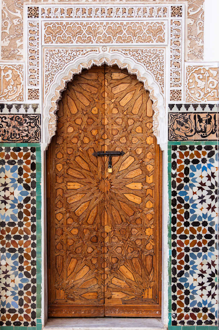 A beautifully ornate wooden door with intricate carvings and patterns, set against a backdrop of colorful mosaic tiles, creating a visually striking architectural feature.
