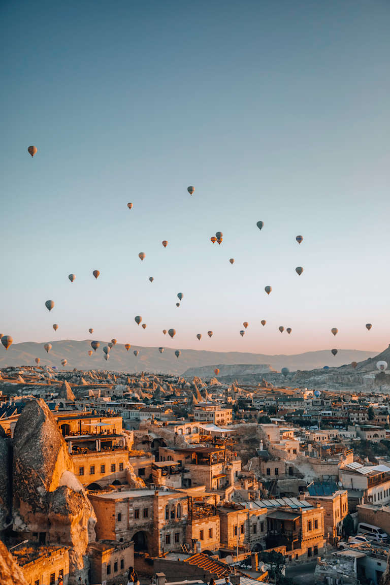 A picturesque cityscape with a stunning array of hot air balloons floating against a vibrant sky, overlooking the rooftops and buildings of the historic town below.