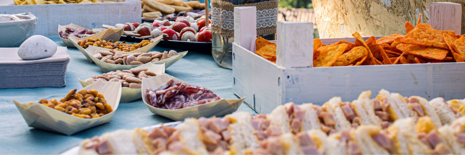 Buffet di catering apparecchiato all'aperto, con coni di patatine, spiedini di caprese, salumi e tramezzini