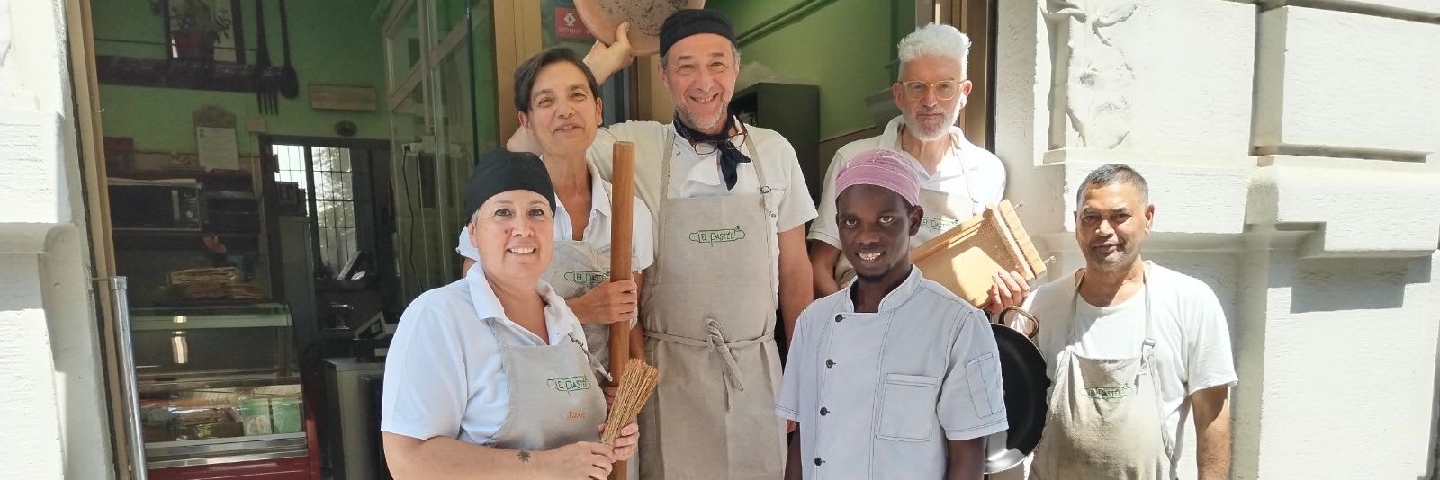 La squadra di El Pastèe davanti al negozio, in grembiule, con mattarello e mazzo di spaghetti
