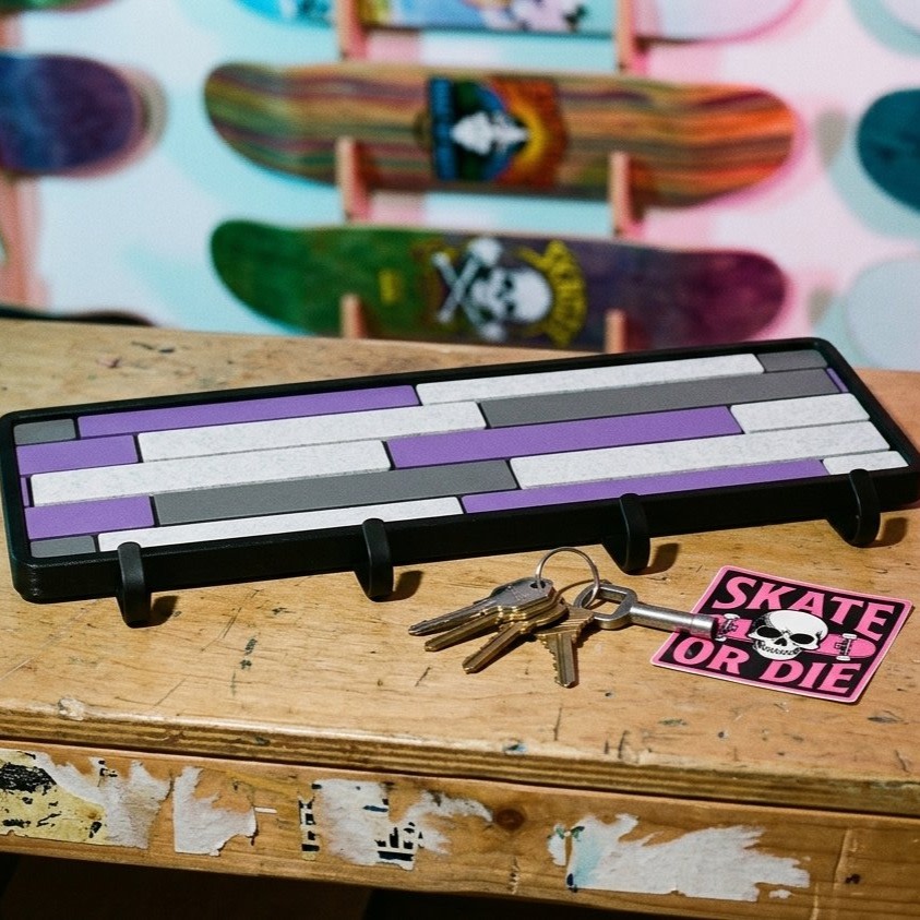Purple Mosaic key holder on a worn wooden bench with loose keys and a skull sticker, skateboard decks racked behind