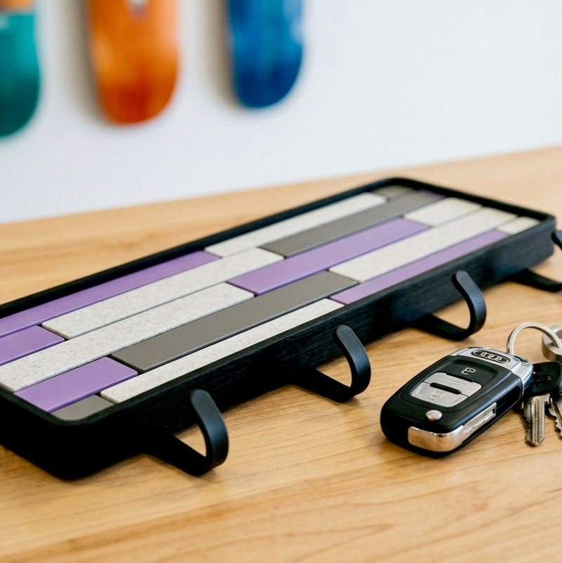 Purple Mosaic key holder in close-up on a wood tabletop, showing the black frame edge and hooks beside a car key fob