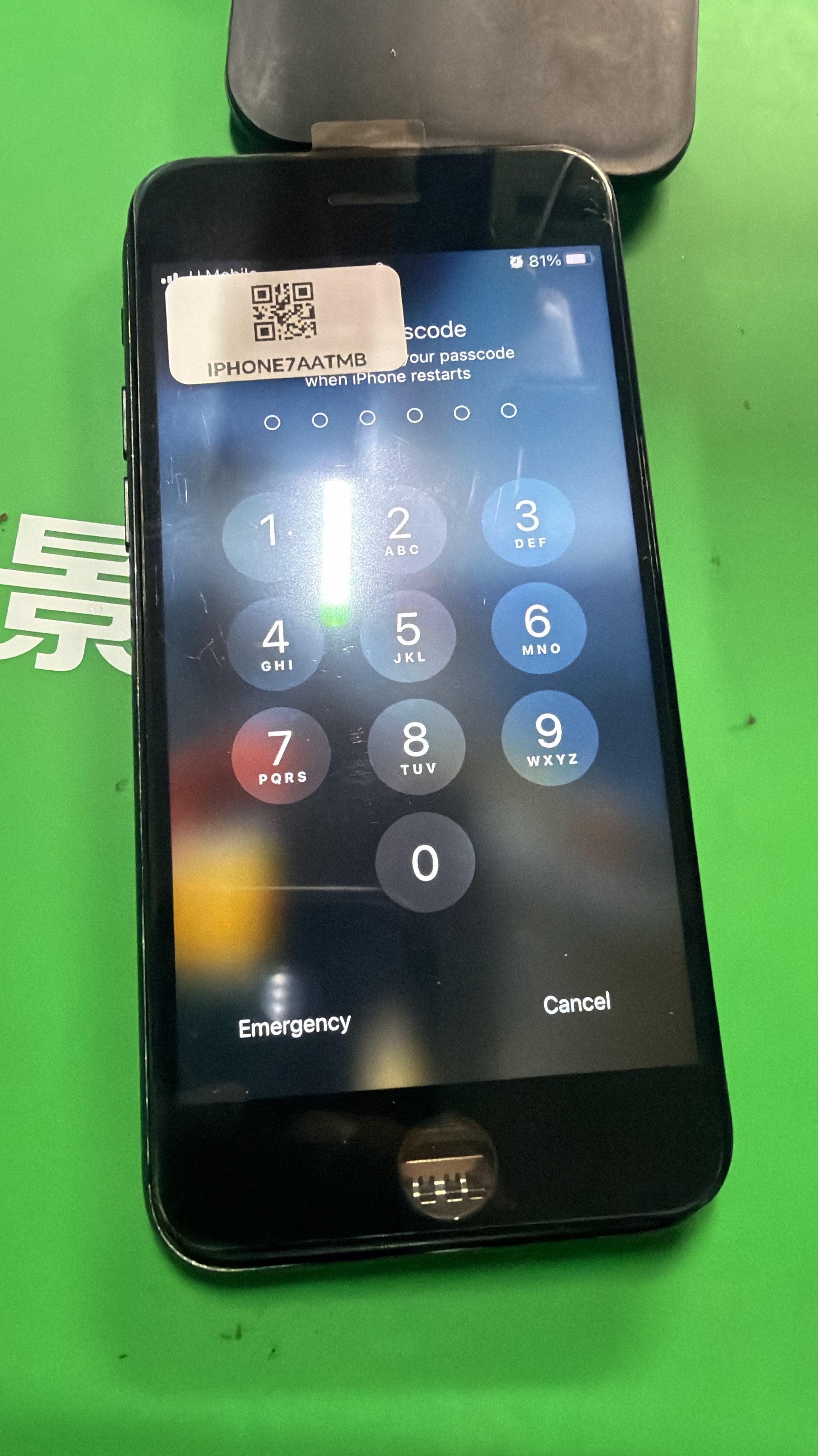 iPhone dengan skrin kod laluan menyala di atas alas kerja hijau