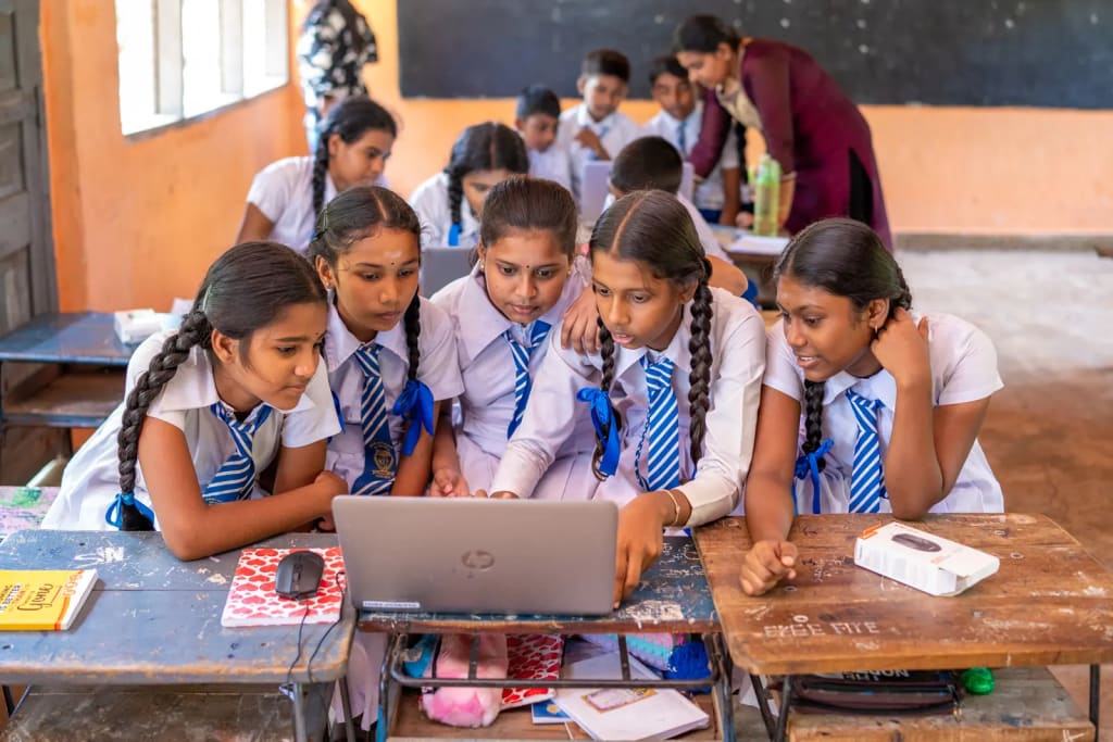 A group of students gathered around one laptop, with a facilitator behind them.